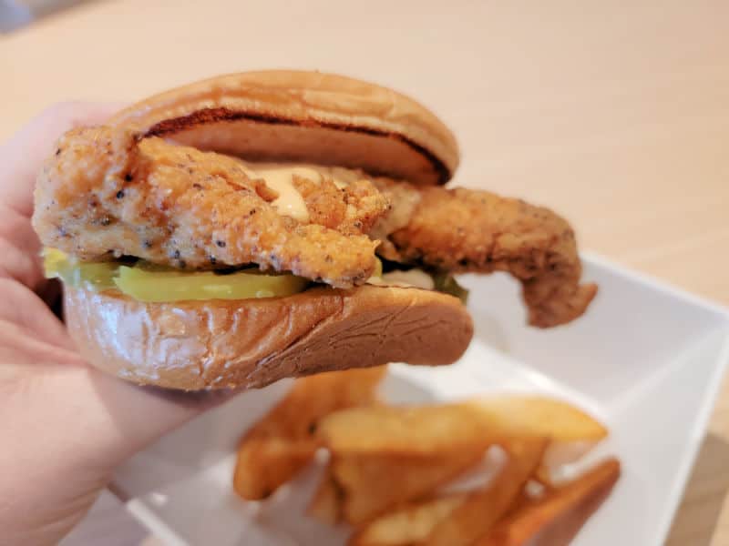 Hand holding a chicken sandwich with pickle and Shaq sauce over a bowl of fries