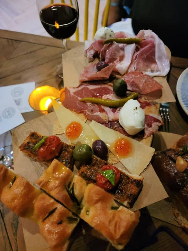 Glass of wine next to an antipasto platter with bread and meats. 