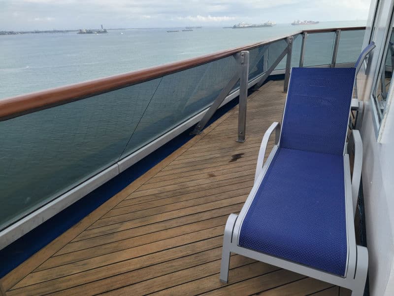 Lounge chair on a wrap around balcony deck with ships and ocean in the background