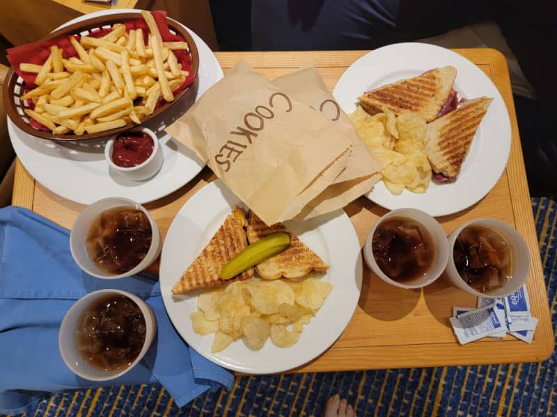 wooden tray with sandwiches, and bags of cookies next to iced tea