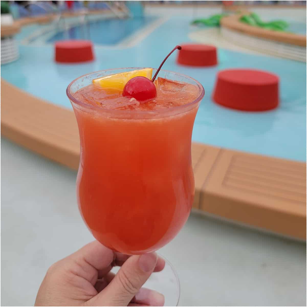 Red tropical cocktail being held near a pool