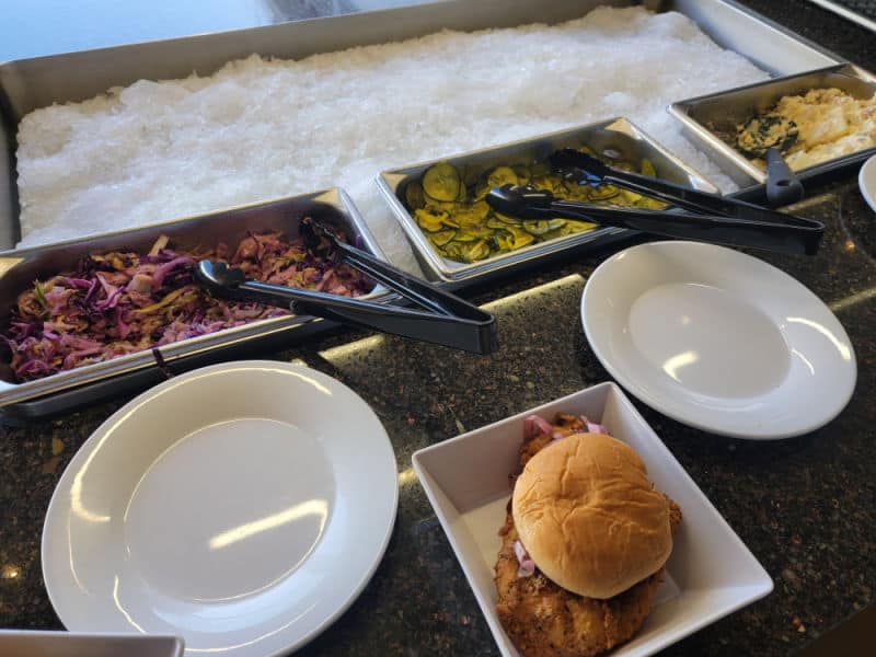 counter with slaw, pickles, and potato salad next to white plates