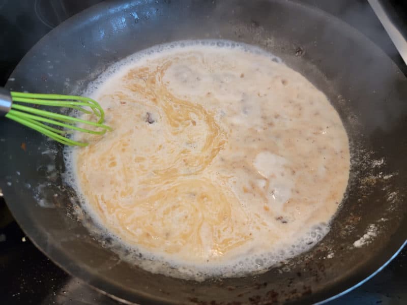 milk adding to bacon grease and flour for bacon gravy in a dark skillet