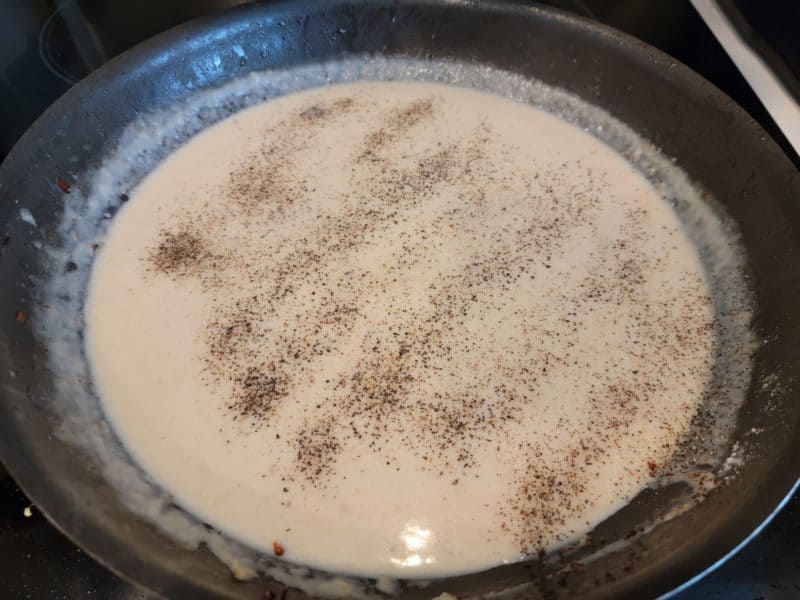  black pepper sprinkled over bacon gravy in a dark skillet