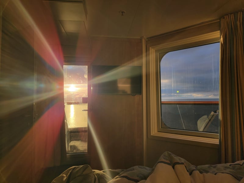 Light coming in a glass door with a window next to it looking out over a balcony to the ocean