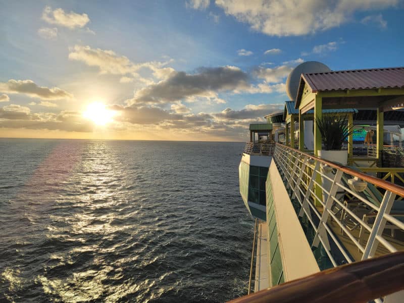 Sunrise in the distance over the ocean looking down the side of a cruise ship