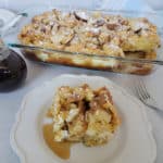 square of overnight French toast on a white plate in front of a casserole dish filled with French Toast casserole