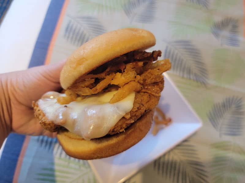 Hand holding a chicken sandwich with cheese on a bun
