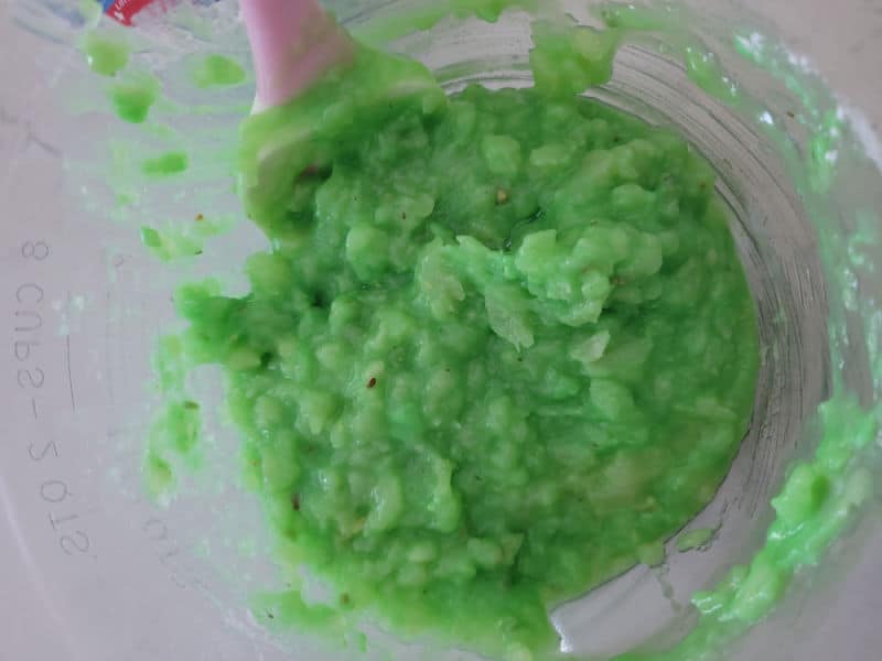 Pineapple and pistachio pudding mixed together in a glass bowl with a spatula for Watergate Salad. 