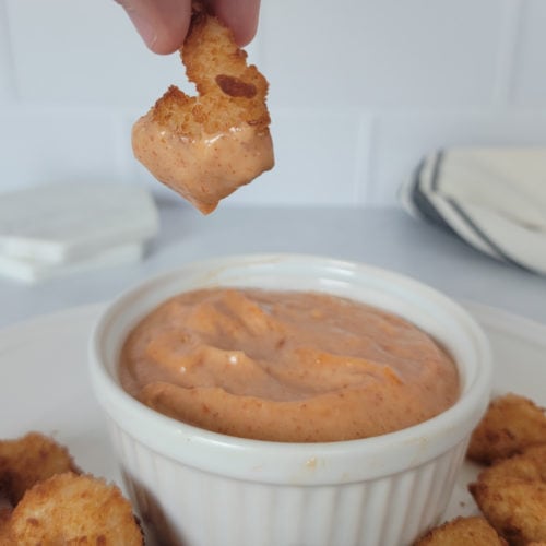 hand holding a shrimp dipping down into a bowl of Yum Yum Sauce