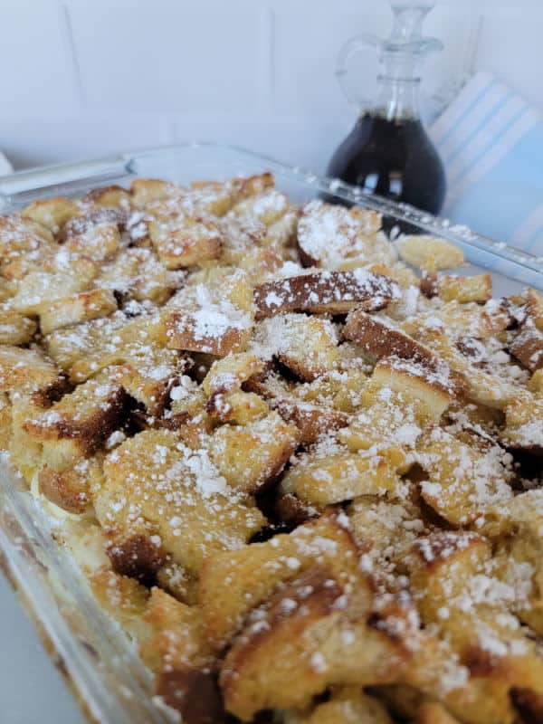 overnight French Toast breakfast casserole in a baking dish with a jar of maple syrup
