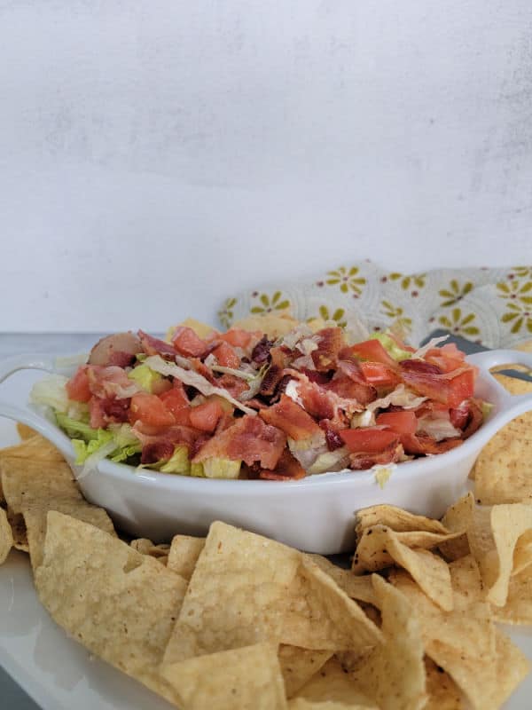 White bowl with bacon, lettuce, and diced tomatoes next to tortilla chips and a cloth napkin 