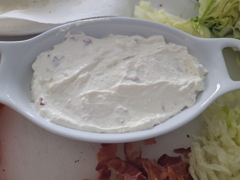 Creamy dip mixture in a white bowl next to bacon and lettuce