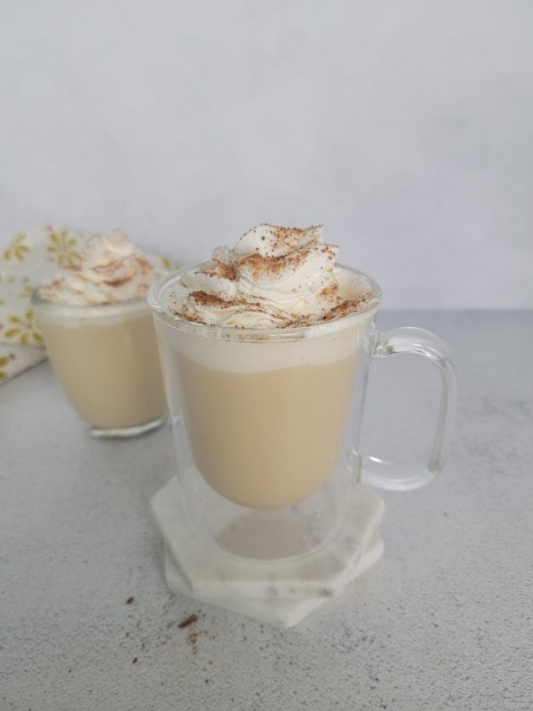 Eggnog Coffee topped with whipped cream and ground cinnamon in a clear glass coffee mug