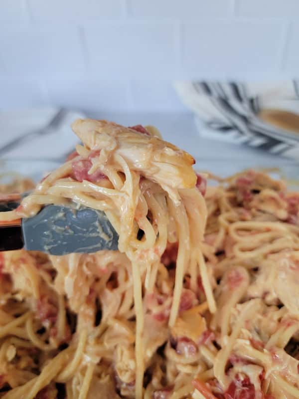 Tongs holding up Rotel Chicken Spaghetti from a full casserole dish