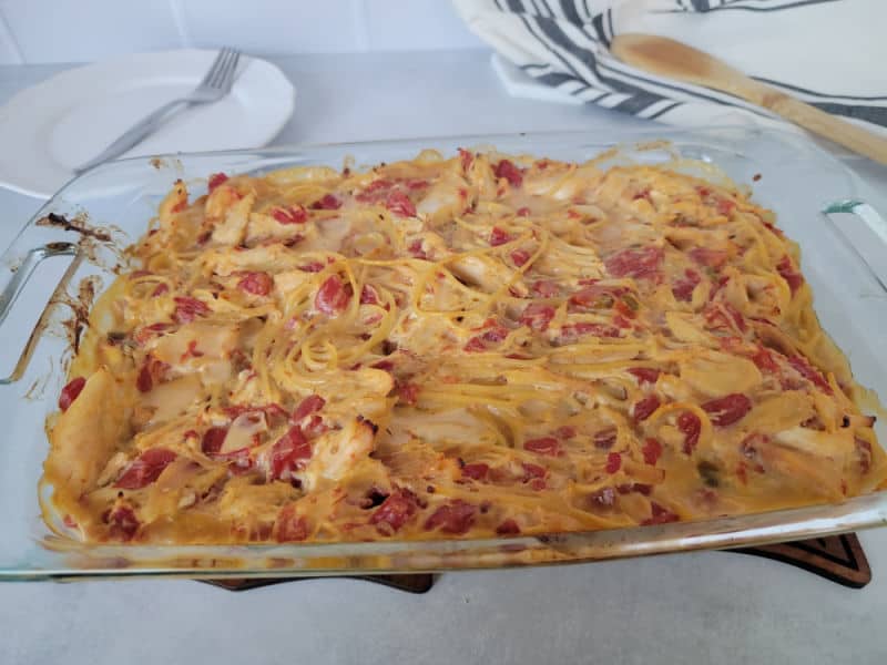 Baked Rotel Chicken Spaghetti in a glass casserole dish next to a wooden spoon