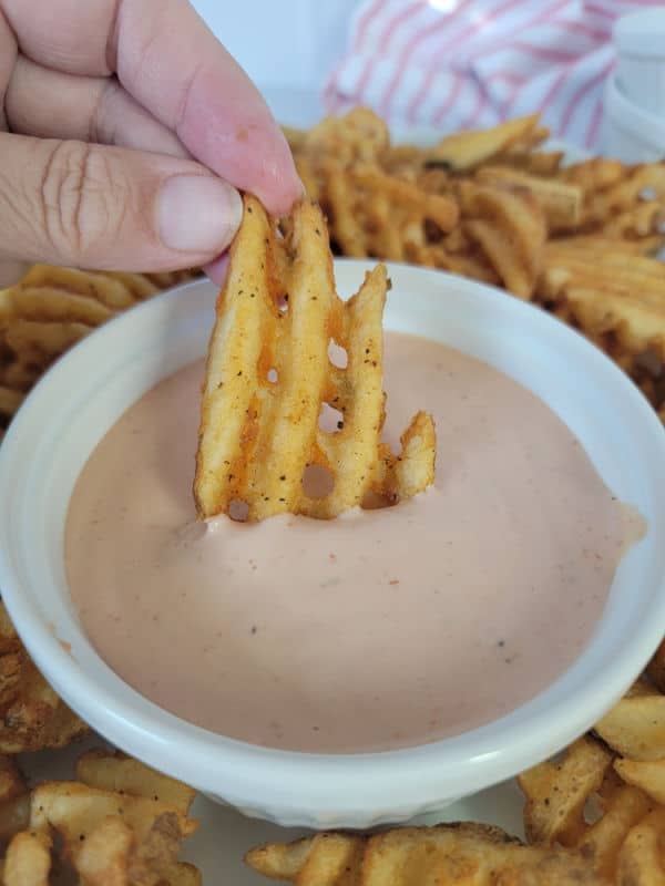 Waffle fry dipping into a bowl of fry sauce