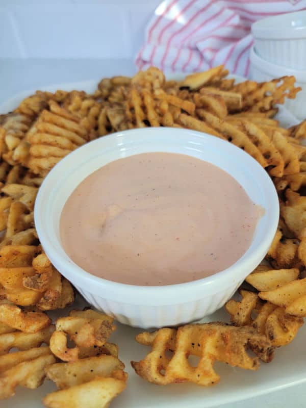 Fry sauce in a white bowl surrounded by waffle fries. 