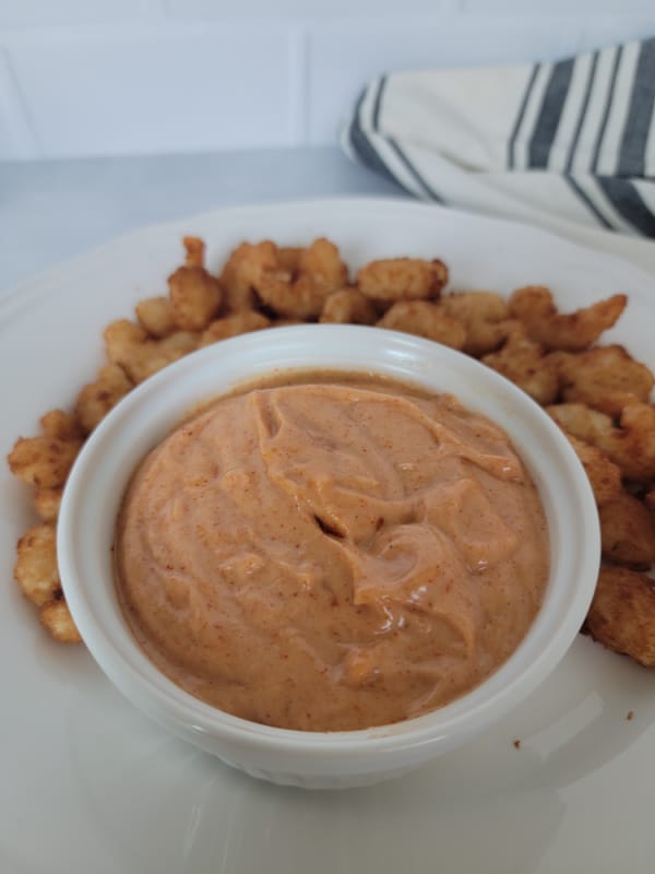 Yum Yum Sauce in a white bowl surrounded by air fryer shrimp on a white plate