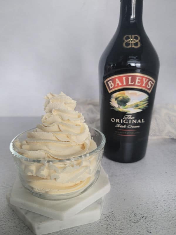 Glass bowl with Baileys whipped cream in it next to a bottle of Baileys Irish Cream. 