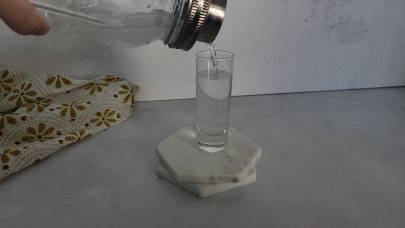 mason jar cocktail shaker pouring clear liquid into a shot glass on two coasters