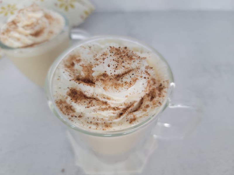Ground cinnamon and nutmeg on top of whipped cream on an eggnog coffee in a clear glass coffee mug