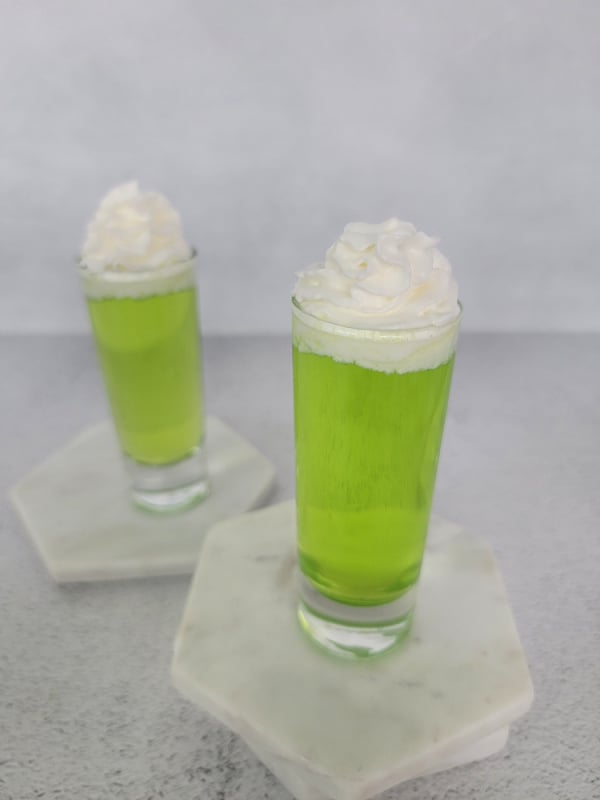 Bright Green Scooby Snack Shot in a glass shot glass garnished with whipped cream