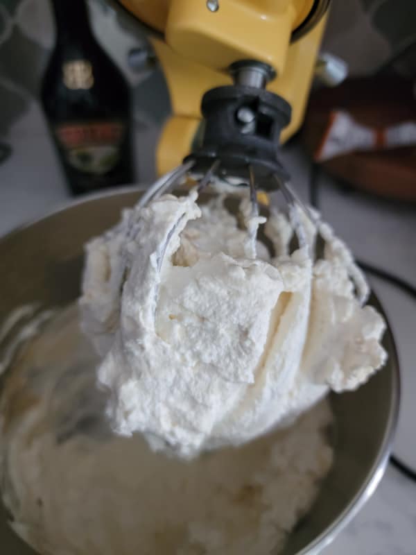 mixer attachment covered in whipping cream above a metal bowl