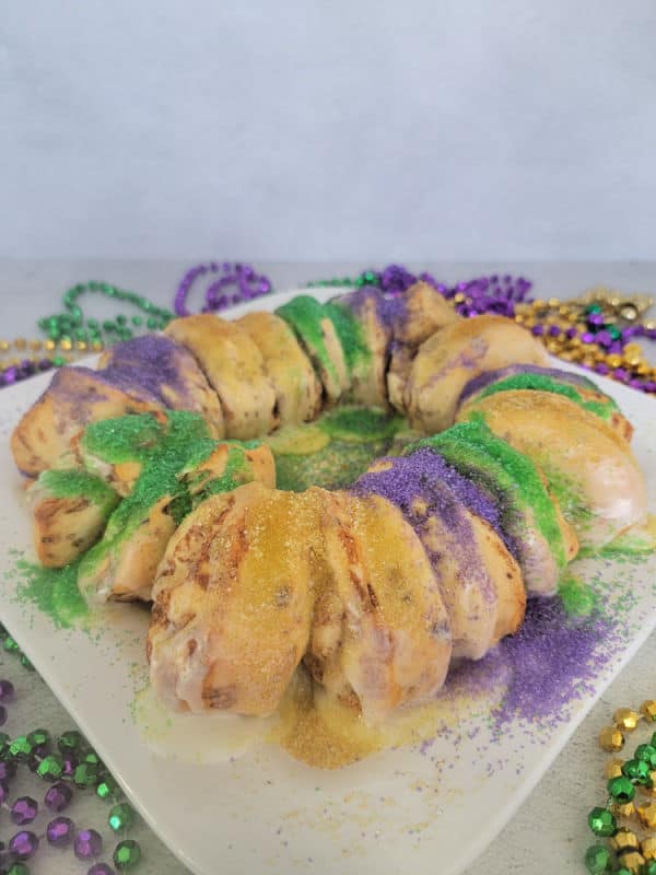 Mardi gras cinnamon roll king cake on a white plate surrounded by mardi gras beads