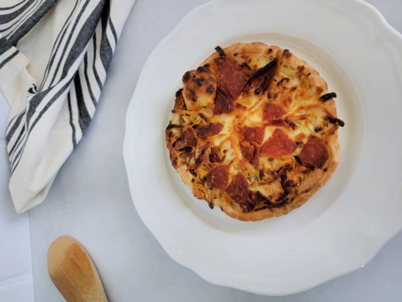 Air fried pepperoni pizza on a white plate next to a cloth striped napkin