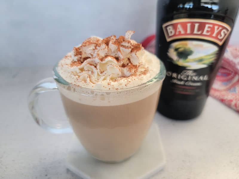 Baileys coffee in a glass coffee mug on a white coaster next to a bottle of Baileys Irish Cream 