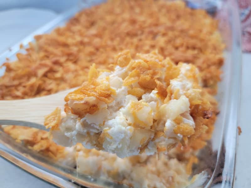 Wooden spoon scooping funeral potatoes from a glass baking dish