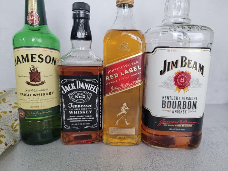 Jameson Irish Whiskey, Jack Daniels Tennessee Whiskey, Johnnie Walker Red Label, and Jim Beam Kentucky Bourbon bottles on a white counter. 
