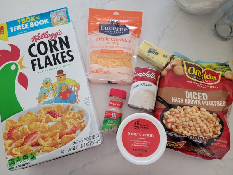 Corn Flakes, Cheddar cheese, cream of potato soup, garlic powder, sour cream, diced hash brown potatoes, and butter on a counter