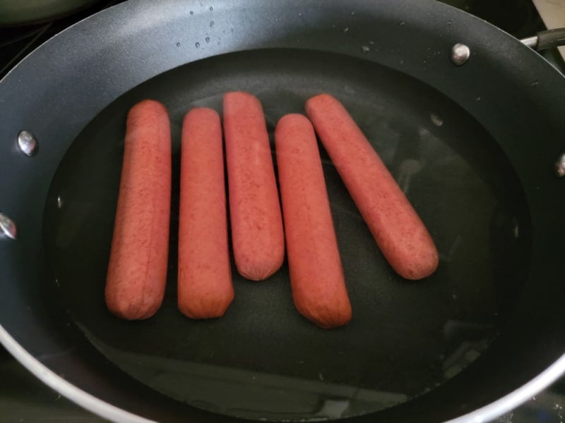Hot dogs in water in a dark skillet pan