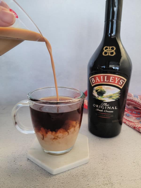 Baileys Irish Cream pouring into a coffee next to a bottle of Baileys