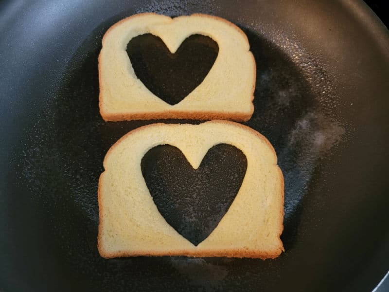 Two pieces of bread with a heart cut out of them in a skillet