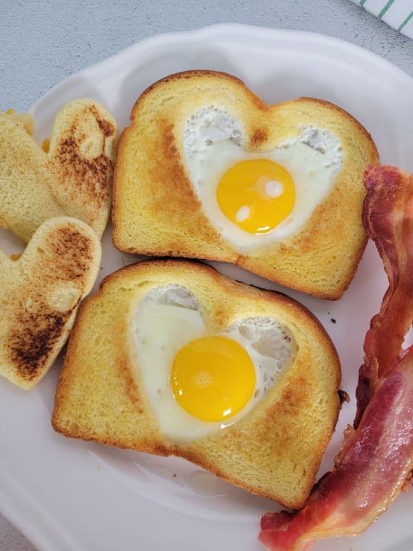 Eggs in a basket toast on a white plate next to bacon