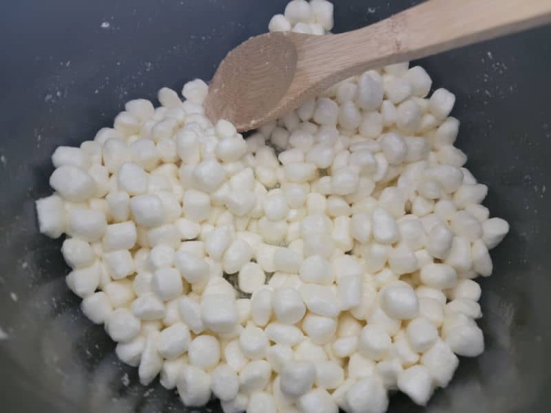 Mini Marshmallows in a dark pot with a wooden spoon for Rice Krispie Treats