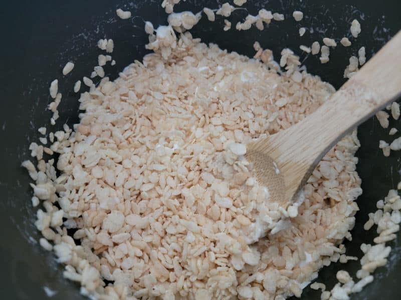 Rice Krispie Cereal and Mini marshmallows in a dark pot with a wooden spoon for Rice Krispie Treats