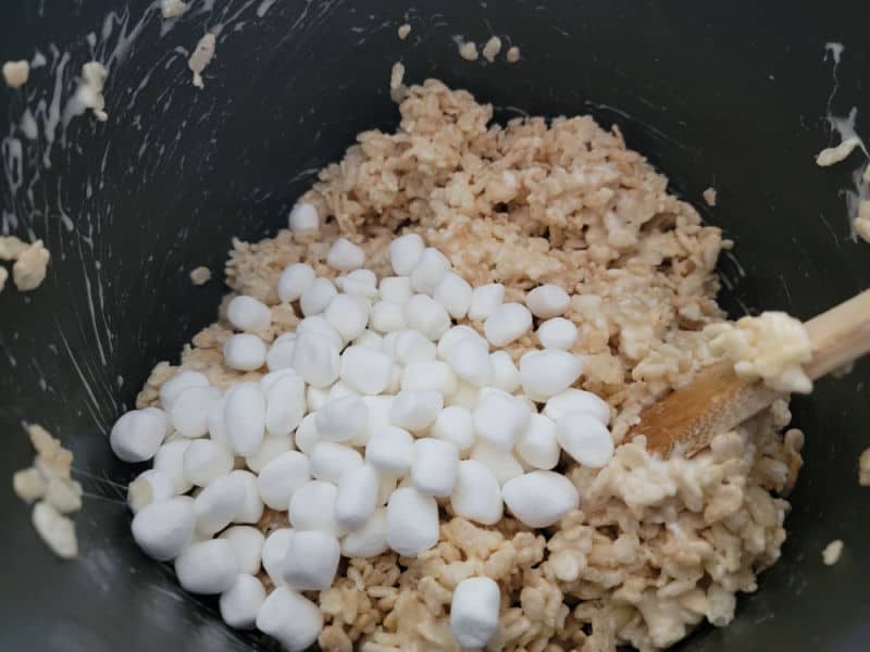 Mini marshmallows on rice krispie cereal in a dark pot for Rice Krispie treats. 