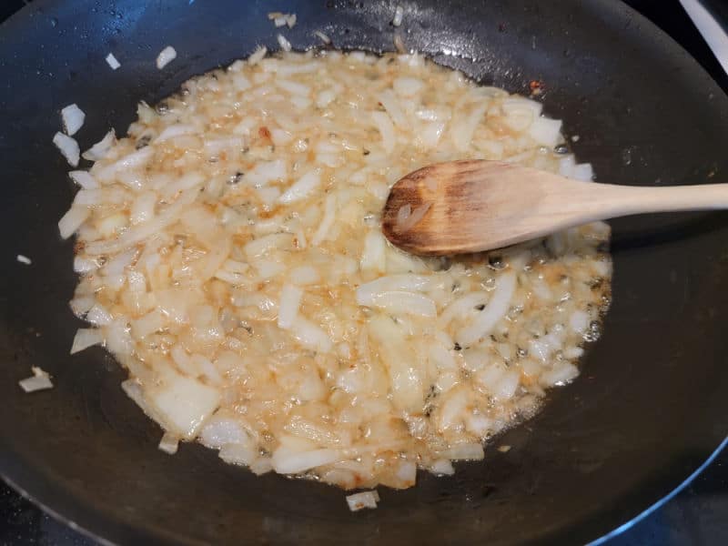 Wooden spoon in onions cooking in bacon grease in a frying pan