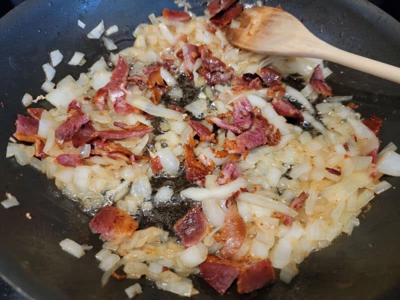 Wooden spoon in a frying pan with bacon and onions