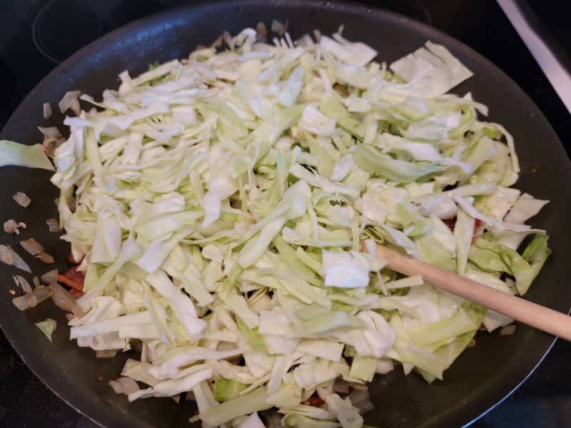 Shredded cabbage in a frying pan with a wooden spoon and bacon