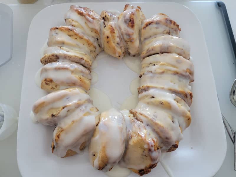 icing covering cinnamon rolls in a circle on a white plate