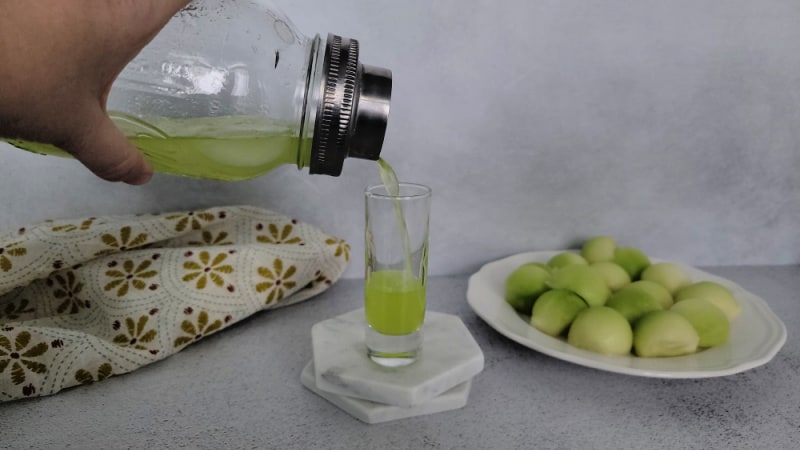 Melon Ball Shot pouring into a shot glass next to a plate of melon