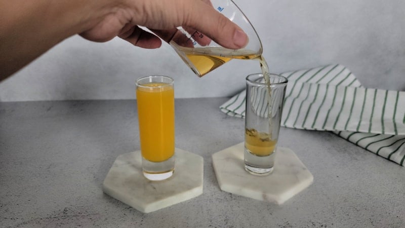 Hand pouring Jameson Irish Whiskey into a shot glass next to a shot glass with orange juice