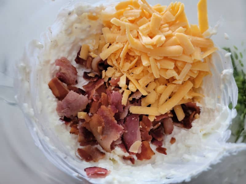 cheddar cheese and bacon pieces on sour cream mix in a glass bowl