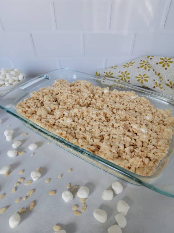 Glass casserole dish filled with the best Rice Krispie Treats surrounded by mini marshmallows and rice cereal on a white counter