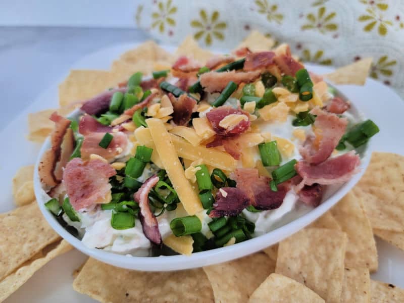 bacon cheddar ranch dip in a white bowl surrounded by tortilla chips 